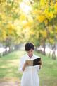 portrait of young beautiful asian woman standing in yellow flowers blooming park summer season and reading a book with happy face emotion