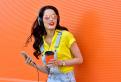 Beautiful smiling woman with headphones listens to music over orange background.  Fashion woman in sunglasses outdoor.