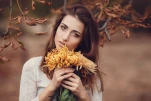 Beautiful young smiling brunette woman with flowers in autumn park