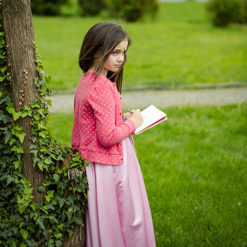 Girl in dress with notebook and pen near tree